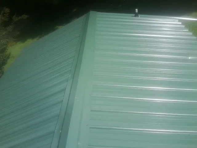 New green metal panels meeting at the ridge of a roof — Flat Roof Repair work by our crew in Mossyrock