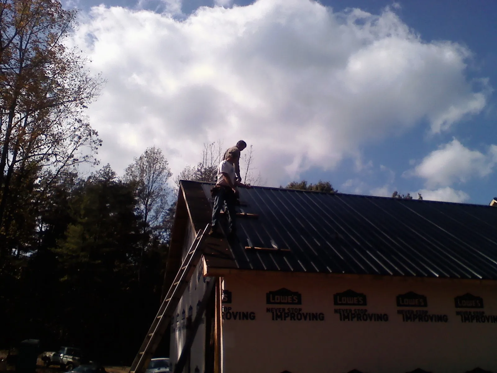 Roofer fastening dark metal panels high against a cloudy sky, from a Roof Inspection job in Mossyrock