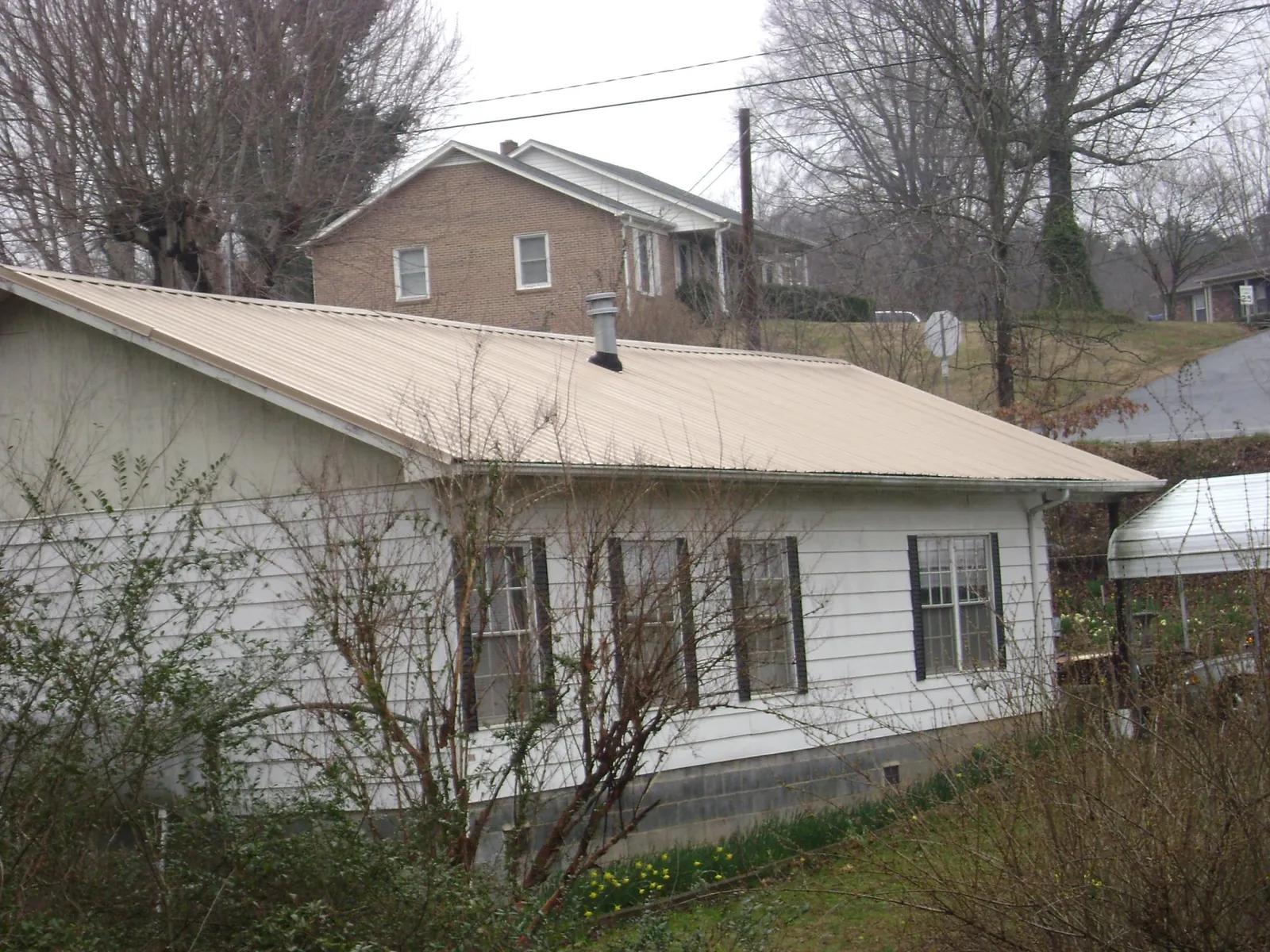 Tan metal roof on a white sided house set into a hillside — Commercial Roofing by Roofing Brothers in Mossyrock
